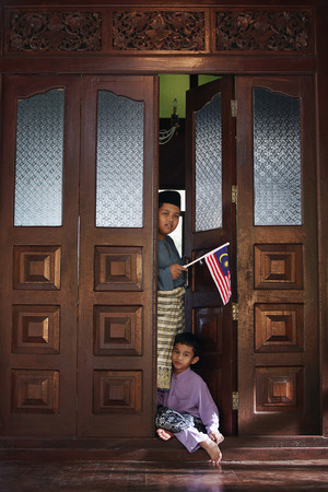 Boy holding flag while another boy is sitting in between the doorwayの写真素材