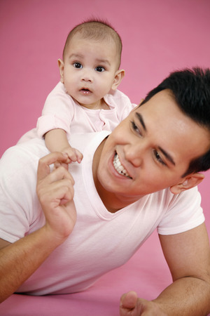 Man giving baby a piggyback ride while lying forward on the floorの写真素材