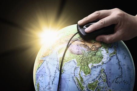 Hand using computer mouse on a globeの写真素材
