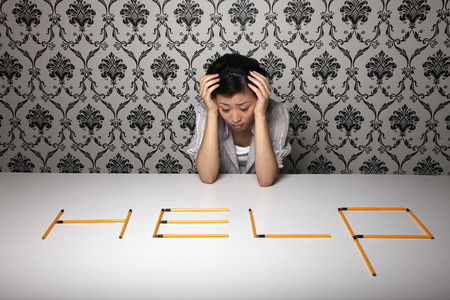 Woman with head in hands looking at 'Help' word arranged from pencils