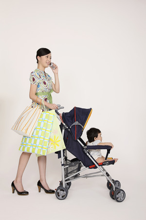 Woman talking on the phone while pushing baby girl in strollerの写真素材