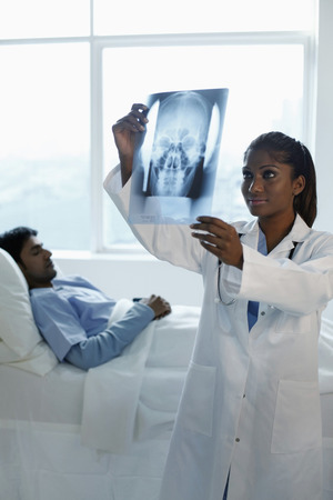 Doctor looking at x-ray with patient sleeping in the backgroundの写真素材