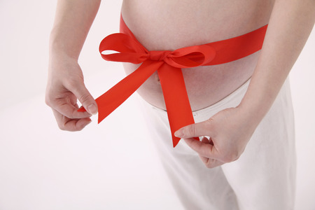 Pregnant woman tying red ribbon around her stomachの写真素材
