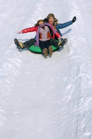 Man and woman sliding down snowy hill on inner tubeの写真素材
