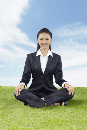 Young Asian businesswoman sitting cross-legged outdoorsの写真素材