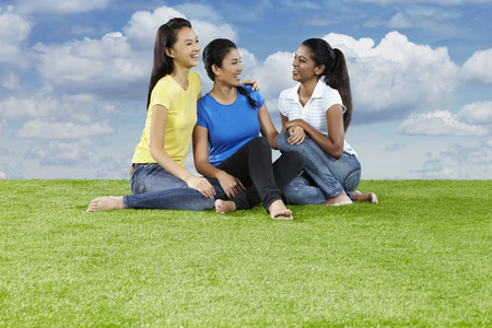 Three young women sitting on the grass, chattingの写真素材