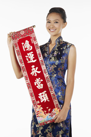 Woman in cheongsam holding banner with Chinese New Year greetingsの写真素材