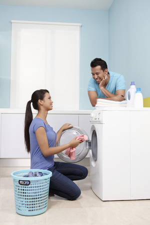 Woman putting clothes into washing machine, man watchingの写真素材