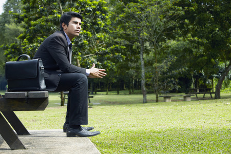 Young Asian businessman sitting on a park benchの写真素材