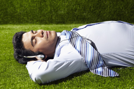 Young Asian businessman with headphones lying on grass の写真素材