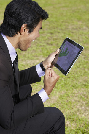 Young Asian businessman sitting on a park bench using a digital tabletの写真素材