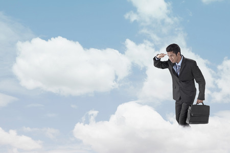 Young businessman standing on clouds, looking belowの写真素材