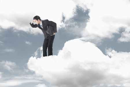 Young businessman standing on clouds, looking belowの写真素材