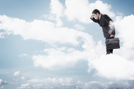 Young businessman standing on clouds, looking belowの写真素材