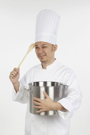 Asian chef holding a stew pot and a wooden spoon, looking stressedの写真素材