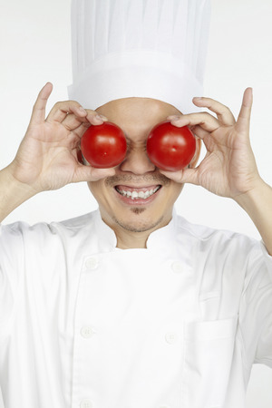 Asian chef holding tomatoes in front of eyesの写真素材
