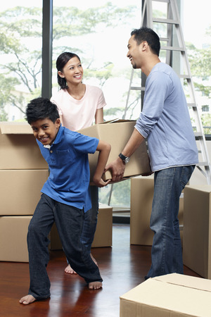 Boy helping parents lifting cardboard box togetherの写真素材