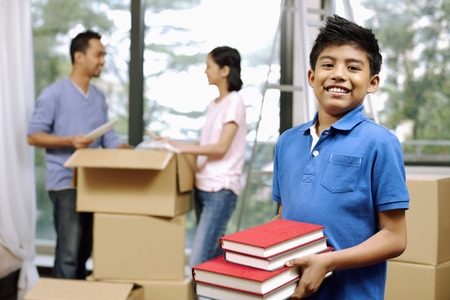 Boy with a stack of books, man and woman packing in the backgroundの写真素材
