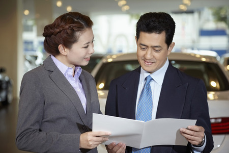 Sales representative explaining to customer specifications of the car form a brochureの写真素材