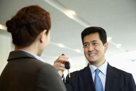Sales representative handing over keys to customer in car showroomの写真素材