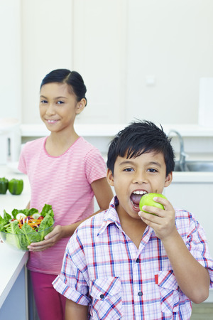 Girl with a bowl of salad while boy is eating green appleの写真素材