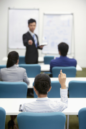 Businessman giving presentation to colleagues, businesswoman raising handの写真素材