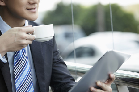 Businessman drinking coffee while using digital tabletの写真素材