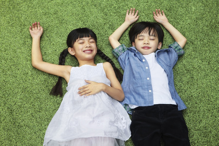 Boy and girl lying down on the grassの写真素材