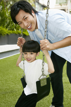 Father pushing son on the swingの写真素材