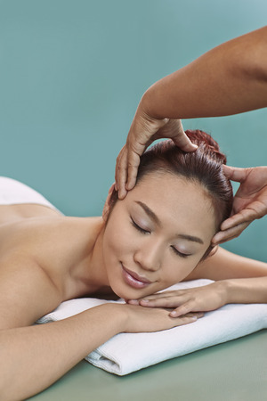 A young woman lying on her front receiving a head massageの写真素材