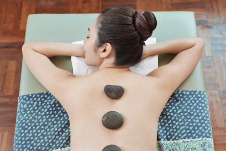 A young woman lying on her front relaxing with massage stone on her backの写真素材