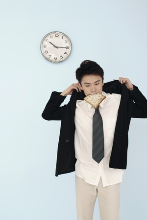 Man biting on bread while putting on his suitの写真素材