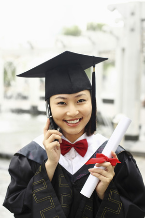 Woman in graduation robe talking on the phoneの写真素材