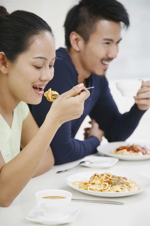 Woman eating spaghetti, man drinking coffee in the backgroundの写真素材