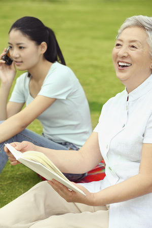 Senior woman holding book and laughing while woman is talking on the phoneの写真素材