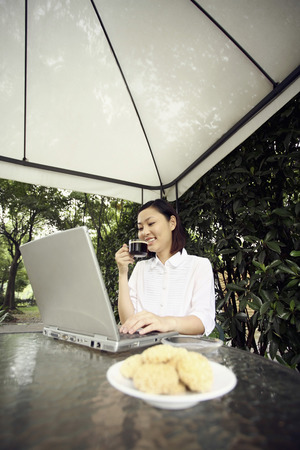 Businesswoman using laptop while having coffee and cookiesの写真素材
