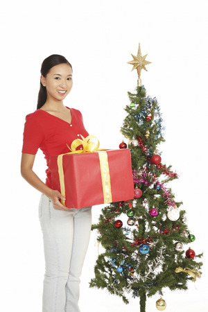 Young woman holding a box of present in front of christmas treeの写真素材