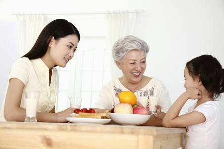 Woman, senior woman and girl having breakfast togetherの写真素材