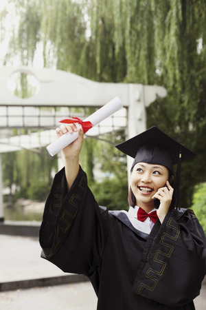 Woman in graduation robe talking on the phoneの写真素材