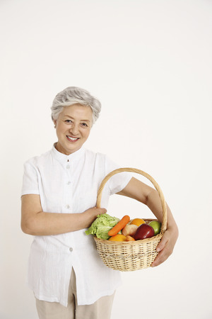 Senior woman holding a basket full of vegetable and fruitsの写真素材