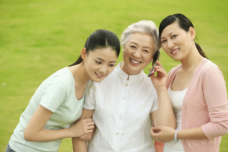 Senior woman talking on the phone, two women standing beside herの写真素材