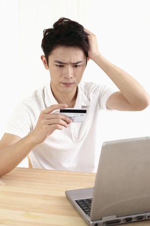 Man frowning and scratching his head while looking at credit cardの写真素材