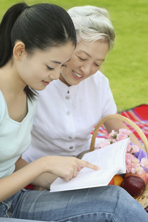 Woman and senior woman reading book togetherの写真素材