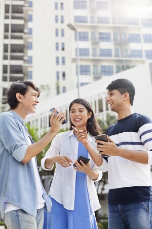Young man showing his mobile phone screen to his friendsの写真素材