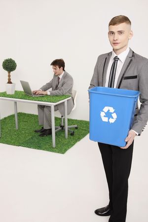 Man holding recycling bin with another man using laptop in the backgroundの写真素材