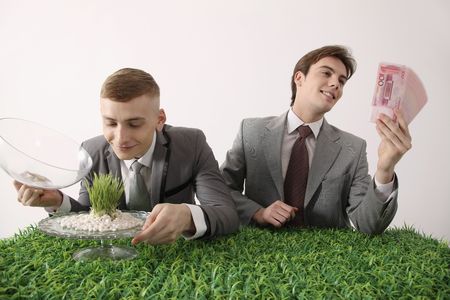 Man admiring grass seedling while another man is admiring moneyの写真素材