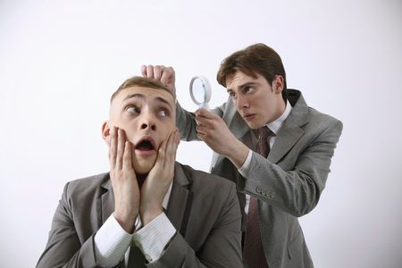 Man examining his friend's hair with magnifying glassの写真素材