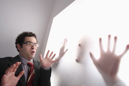 Businessman frowning while looking at silhouette of a man behind transparent paper の写真素材