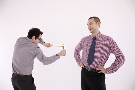 Businessman aiming slingshot at another manの写真素材