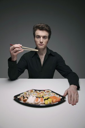 Man holding chopsticks with a plate of sushi on the tableの写真素材